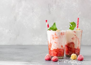 Katmanlı çilekli ve ahududulu smoothie veya naneli, ahududulu ve hindistan cevizli süslemeli milkshake. Kahvaltı veya atıştırmalık sağlıklı yiyecekler..