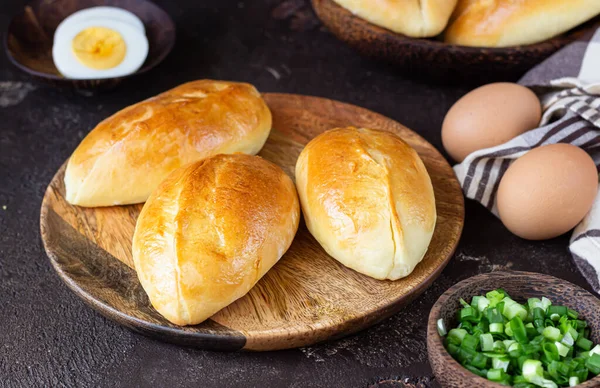 Traditional Russian pies with green onion and egg on wooden plate, rustic background. Russian pirozhki, homemade baked patties.