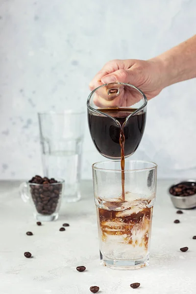 Tonik ve buz küplü, açık gri arkaplanlı uzun bir bardağa espresso dökmek. Tonik buzlu kahve yapıyorum. Yaz içeceği..