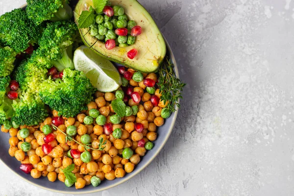 Healthy vegetable lunch of broccoli, roasted chickpeas, avocado, green peas, pomegranate seeds, lime and mint on a ceramic plate. Vegan food, clean eating or dieting concept.