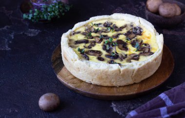 Tuzlu tart, turta ya da mantarlı kiş ve ahşap tabakta peynir, koyu kahverengi arka plan. Ev yapımı lezzetli sonbahar pastanesi..