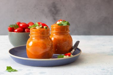 Geleneksel İspanyol çorbası, salatalık ve domates garnitürlü. Cam kavanozlarda ev yapımı soğuk domates kremalı çorba. Gri arkaplan.