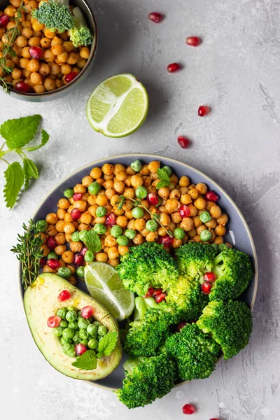 Healthy vegetable lunch of broccoli, roasted chickpeas, avocado, green peas, pomegranate seeds, lime and mint on a plate. Vegan food, clean eating or dieting concept. Top view.