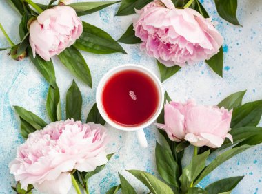Mavi taştan arka planda bir fincan çay ve pembe şakayık çiçeği. Kopyalama alanı olan üst görünüm. Kadın ya da Anneler Günü hediyesi.