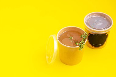 Sebze ya da tavuk buğulama suyu ya da kekik soslu et suyu sarı arka planda tek kullanımlık kağıt bardakta. Çorba hazır, sağlıklı yemek servisi..