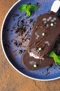 Mavi seramik tabakta naneli çikolatayla kaplı dondurma. Koyu dokulu arkaplan.