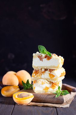 Tahta tahtada parçalanmış, koyu arkaplanlı lezzetli, çiğ kayısılı peynirli kek. Sağlıklı vejetaryen gıda kavramı.