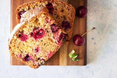 Kesme tahtasının üzerinde kiraz ve fındıklı ev yapımı pastanın dilimleri. Açık mavi taş arka plan. Üst görünüm.