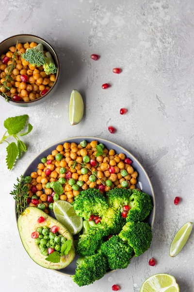 Healthy vegetable lunch of broccoli, roasted chickpeas, avocado, green peas, pomegranate seeds, lime and mint on a ceramic plate. Vegan food, clean eating or dieting concept.
