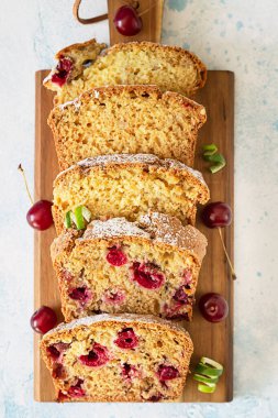 Tahta kesme tahtasının üzerinde kirazlı ve fındıklı ev yapımı pastanın dilimleri. Açık mavi arkaplan. Üst görünüm.