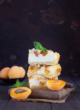 Tahta kesme tahtasının üzerinde parçalanmış kayısılı leziz bir cheesecake. Eski, koyu bir arka plan. Sağlıklı vejetaryen gıda kavramı.