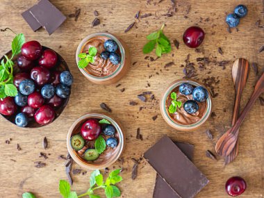 Çikolatalı kremalı porsiyon kavanozlar ya da tatlı kiraz, yabanmersini ve nane şekeri ile süslenmiş puding ve bir parça koyu çikolata. Seçici odaklanma. Kırsal tarzda. Koyu arkaplan.