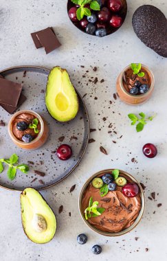 Çikolata parçalı çiğ avokado çikolatalı mus, kiraz, yabanmersini ve nane aromalı, seçici odaklı. Gri taş arka plan. Sağlıklı vejetaryen çikolatalı tatlı.