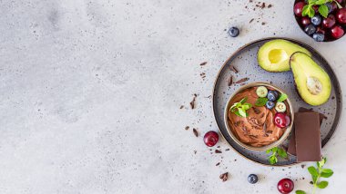 Çikolata parçalı çiğ avokado çikolatalı mus, kiraz, yabanmersini ve nane aromalı, seçici odaklı. Gri taş arka plan. Sağlıklı vejetaryen çikolatalı tatlı.