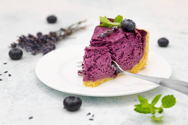 Piece of blueberry or bilberry cheesecake decorated with fresh berries, mint and rosemary. Light grey concrete background. Selective focus.