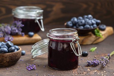 Kahverengi beton arka planda taze böğürtlenli, lavantalı ve biberiyeli tatlı yaban mersini reçeli kompozisyon. Yaz hasat konsepti.