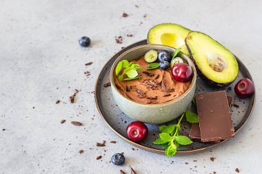 Çikolata parçalı çiğ avokado çikolatalı mus, kiraz, yabanmersini ve nane aromalı, seçici odaklı. Gri arka plan. Sağlıklı vejetaryen çikolatalı tatlı.