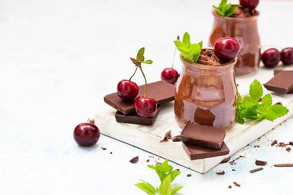 Шоколадний мус з м'ятою і солодкою вишнею в стаканчиках на дерев'яній обробній дошці. Світло-синій фон . — стокове фото