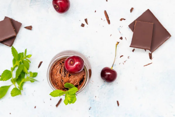 Домашній темно-шоколадний мус прикрашений солодкою вишнею та м'ятою та шматочками шоколаду на світло-блакитному фоні . — стокове фото