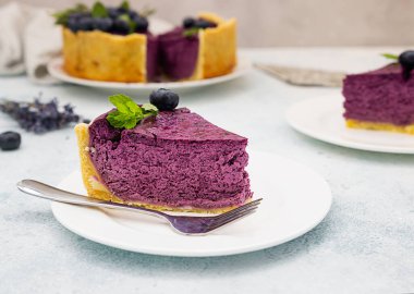 Taze böğürtlen, nane ve biberiye ile süslenmiş yabanmersinli ya da çilekli cheesecake. Açık gri beton arka plan. Seçici odak.