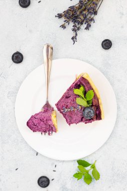 Taze böğürtlen, nane ve biberiye ile süslenmiş yabanmersinli ya da çilekli cheesecake. Açık gri beton arka plan. Seçici odak.