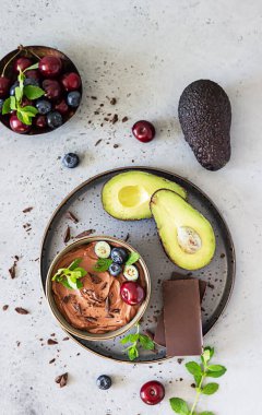 Çikolata parçalı çiğ avokado çikolatalı mus, kiraz, yabanmersini ve nane aromalı, seçici odaklı. Gri taş arka plan. Sağlıklı vejetaryen çikolatalı tatlı.