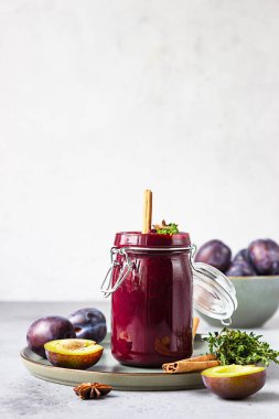 Baharatlı erik reçeli kavanozu, tarçın, anason yıldızı ve gri taş zemin üzerinde kekik içeren kompozisyon.