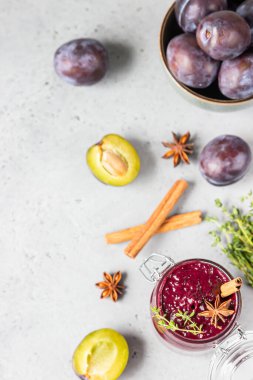 Baharatlı erik reçeli kavanozu, tarçın, anason yıldızı ve gri taş zemin üzerinde kekik içeren kompozisyon.