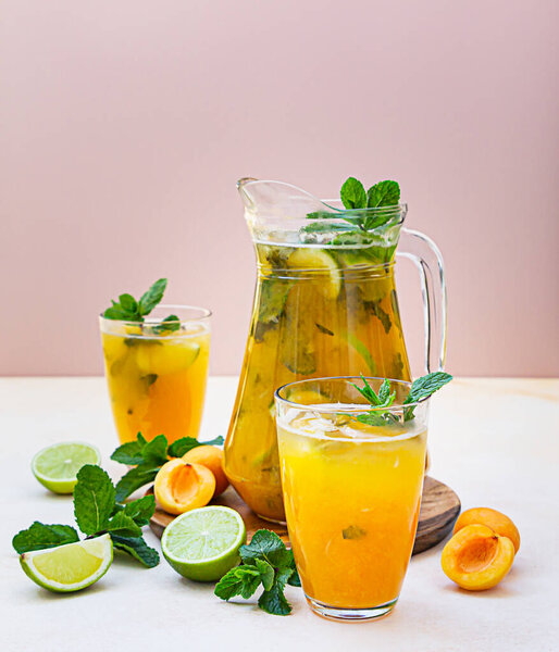 Абрикосовый коктейль или чай со льдом со свежей мятой, лаймом и абрикосами. Летний освежающий холодный напиток. Светлый фон.