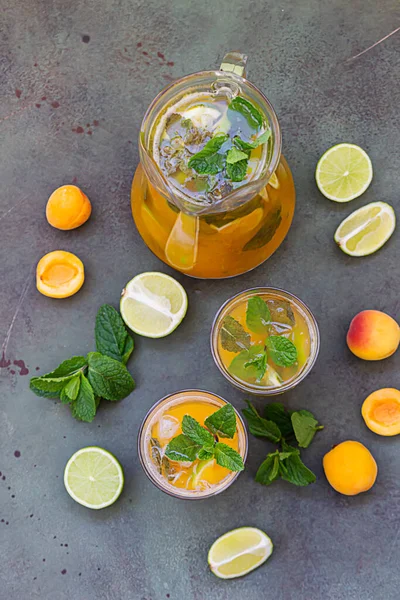 Köstliches Erfrischungsgetränk mit Aprikose, Limette und Minze in Krug und Gläsern auf grünem Hintergrund. — Stockfoto