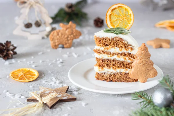 Christmas or New Year gingerbread cake with white cream decorated with gingerbread cookies, fir tree branches, cones, spices and dried orange slice. Winter cake. Grey concrete background.