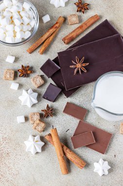 Koyu ve sütlü çikolata, tarçın, anason yıldızı, esmer şeker, lokum, krema ve süt. Sıcak çikolata yapmak için gerekli malzemeler. Üst görünüm.