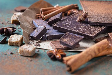 Koyu ve sütlü çikolata parçaları, kakao tozu, tarçın, anason yıldızı ve taş zemin üzerinde esmer şeker. Şekerleme dükkanı reklamcılığı ve yemek malzemeleri konsepti.