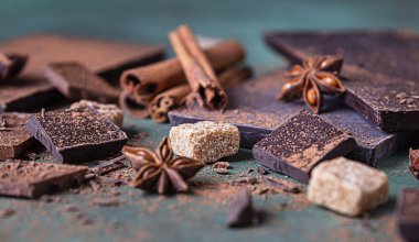 Koyu ve sütlü çikolata parçaları, kakao tozu, tarçın, anason yıldızı ve taş zemin üzerinde esmer şeker. Şekerleme dükkanı reklamcılığı ve yemek malzemeleri konsepti.