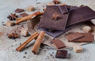 Koyu ve sütlü çikolata parçaları, kakao tozu, tarçın, anason yıldızı ve taş zemin üzerinde esmer şeker. Şekerleme dükkanı reklamcılığı ve yemek malzemeleri konsepti.