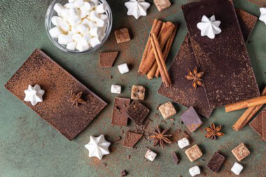 Sıcak çikolata yapmak için gerekli malzemeler. Koyu ve sütlü çikolata, kakao tozu, tarçın, anason yıldızı, esmer şeker, marşmelov, krema ve süt yeşil taş zemin üzerinde.