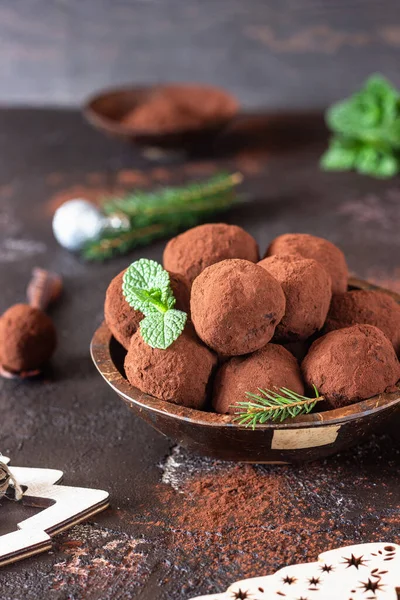 Dark chocolate truffles with raw cocoa powder, mint and fir tree branches, dark brown background. Christmas composition.