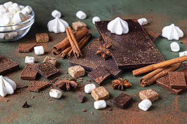 Sıcak çikolata yapmak için gerekli malzemeler. Koyu ve sütlü çikolata, kakao tozu, tarçın, anason yıldızı, esmer şeker, krema ve süt yeşil arka planda..