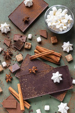Sıcak çikolata yapmak için gerekli malzemeler. Koyu ve sütlü çikolata, kakao tozu, tarçın, anason yıldızı, esmer şeker, marşmelov, krema ve süt yeşil taş zemin üzerinde.
