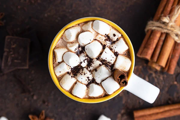 Twee witte keramische kopjes met warme cacao of chocolade met marshmallow en anijs, kaneel en bittere chocolade op donkerbruine stenen ondergrond. — Stockfoto