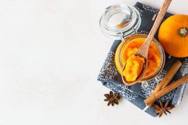 Cam kavanozda organik balkabağı püresi ve taze kabaklı ahşap kaşık ve keten peçetede baharatlar. Hafif beton arka plan. Boşluğu kopyala.