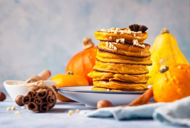 Ballı ve fındıklı yumuşak balkabağı krepleri, mavi arka planda taze balkabakları ve baharatlar..
