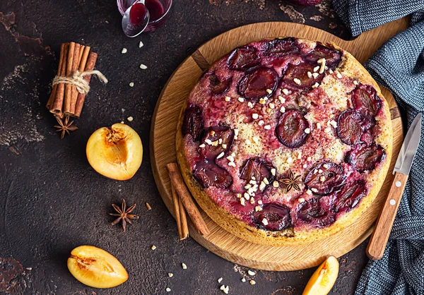 Homemade sweet plum pie or cake with nuts and spices on wooden board, dark brown stone background. Fruit pie. Rustic style. Selective focus.