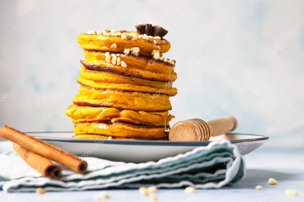 Stack of delicious pumpkin fluffy pancakes with maple syrup or honey and nuts. Healthy breakfast. Autumn food. Blue background.