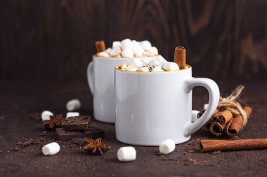 Sıcak kakaolu iki beyaz seramik bardak ya da kremalı çikolata, tarçın ve koyu taşlı arka planda acı çikolata..