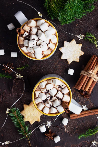 Hot chocolate or cocoa with marshmallow and cinnamon, shortcrust cookies, spices and bitter chocolate on dark background. Festive Christmas or New Year decoration.