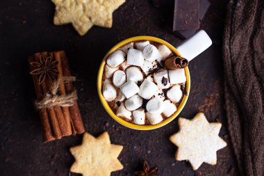 Sıcak kakaolu iki beyaz seramik bardak ya da kremalı çikolata, tarçın ve koyu kahverengi taşlı arka planda acı çikolata..