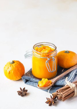 Cam kavanozda organik balkabağı püresi ve taze kabaklı ahşap kaşık ve keten peçetede baharatlar. Hafif arkaplan.