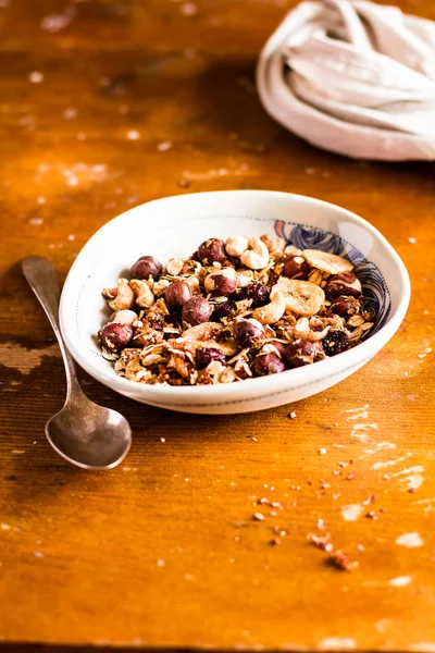 Super bowl of granola or muesli with toasted oat flakes, banana chips, cashew nuts, hazelnuts on a wooden table, selective focus. Food for breakfast or snack. Healthy and organic food.