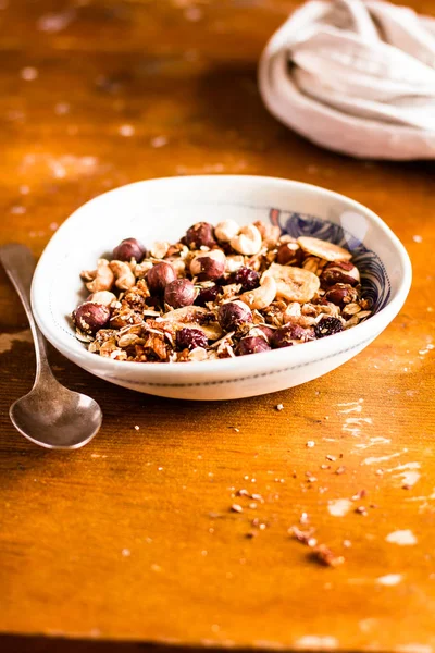 Super bowl of granola or muesli with toasted oat flakes, banana chips, cashew nuts, hazelnuts on a wooden table, selective focus. Food for breakfast or snack. Healthy and organic food.